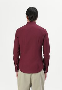 Bordeaux langwerpig shirt met een moderne pasvorm, puntkraag en met knopen afgesloten manchetten. Gladde stof met een subtiele glans en een rug yoke-detail.