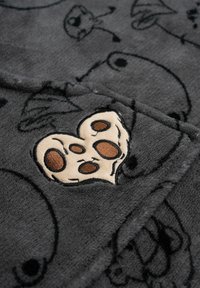 Tessuto felpato grigio con un'applicazione testurizzata a forma di cuore con macchie marroni, circondata da motivi astratti. Aspetto morbido e accogliente.