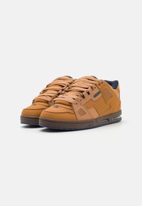 Tan leather sneakers with a textured finish, padded collar, and blue accents. Features thick laces and a rubber outsole for grip.