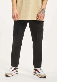 Svarte cargo bukser med sidelommer, tapered passform, laget av slitesterkt stoff. Kombinert med flerfargede sneakers med hvite, svarte og røde detaljer.