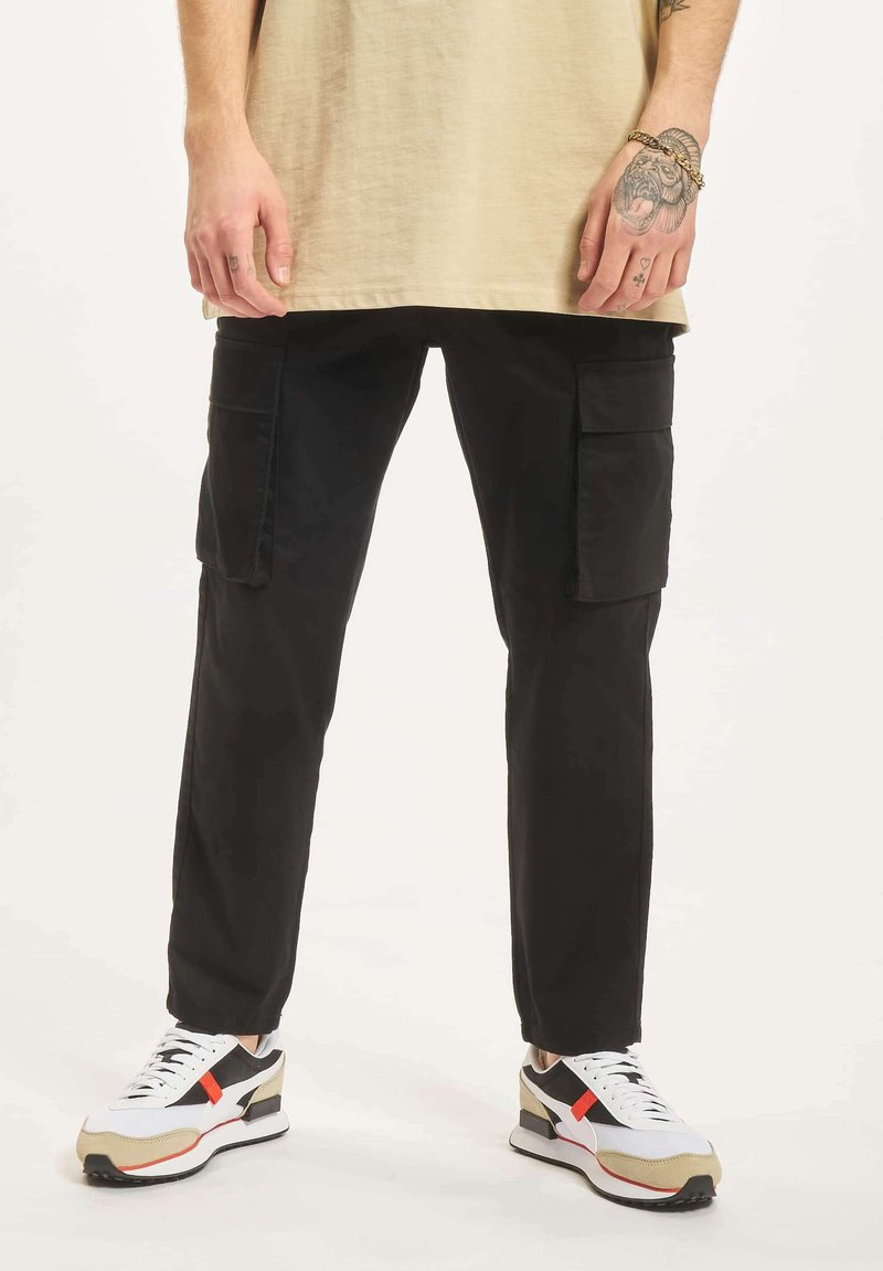 Svarte cargo bukser med sidelommer, tapered passform, laget av slitesterkt stoff. Kombinert med flerfargede sneakers med hvite, svarte og røde detaljer.
