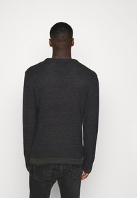 Ciemnogranatowy sweter dziany z teksturowanym wzorem, zaokrąglonym dekoltem i prążkowanym zakończeniem, zestawiony z czarnymi dżinsami.