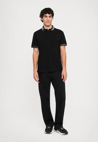 Sort polo t-shirt med mønstret krave, parret med sorte bukser med hvid syning, båret med sorte sportsko.