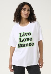 T-shirt oversize blanc mettant en avant un texte noir en gras "Vivre Aimer Danser" avec des accents verts, à manches courtes et à encolure ronde.