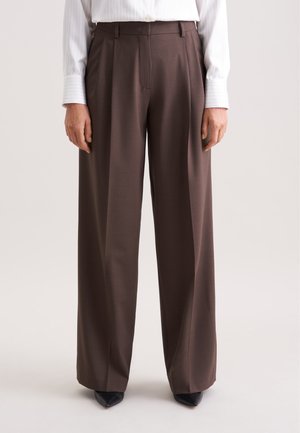 Brune high-waisted bukser med bred benprofil, dekoreret med læg og en glat tekstur. Sammen med spidse sorte sko.