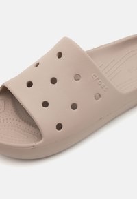Sandalo scivoloso beige con fori intagliati, realizzato in materiale morbido. Presenta una soletta testurizzata per il comfort e un logo stampato sul lato.