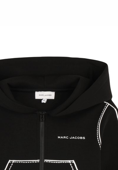 Sweat à capuche noir avec fermeture éclair, surpiqûres blanches et le nom de la marque "MARC JACOBS" imprimé en blanc sur la poitrine.