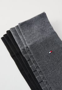 Vier Paar Socken in Schwarz und Grautönen. Mit gerippter Textur und einem kleinen Logo in Rot, Weiß und Blau an der Seite.