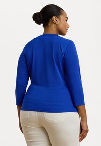 Long-sleeve, fitted top in bright blue fabric with a smooth texture. Features a round neckline and 3/4 length sleeves.