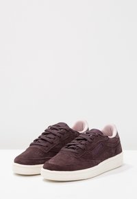 Sneakers gjorda av mörklila mocka med ljusrosa accenter, med en slät tåkappa, texturerade paneler och en krämfärgad gummisula.