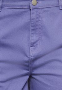 Fialové džíny z denimu s klasickým střihem, viditelnými švy a kulatým kovovým knoflíkem na pásku.