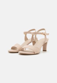 Beige nubukist kõrged sandaalid, millel on üks ette triibuline rihm, pahkluu rihm kuldse kinnitusega ja keskmise blokknõela kõrgus.