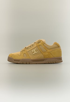 Chaussure de skate DC couleur fauve et beige avec lacets et logo sur le côté, vue de profil sur un fond neutre.