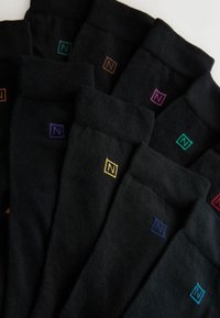 Schwarze Socken mit geripptem Muster, verziert mit kleinen, bunten Logos in verschiedenen Farbtönen (Lila, Orange, Blau, Grün, Gelb und Rosa).