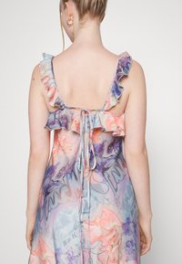 Robe légère et transparente dans des couleurs pastel, ornée de motifs floraux, avec des bretelles volantes et une fermeture à nouer dans le dos. Texture lisse.