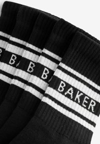 Sorte bomuldsstrømper med hvidstriber og ordet "BAKER" vævet i sort. Ribbet tekstur øverst for bedre greb.