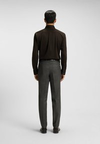Donkerbruine langemouwen shirt met knoopmanchetten, gecombineerd met op maat gemaakte grijs gestructureerde broek en zwarte schoenen. Gezien vanuit de achterkant.