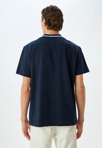 Marineblå kortærmet T-shirt i bomulds materiale med en kontrastfarvet kravekant, løs pasform og ensfarvet bagside. Præsenteret af en model.
