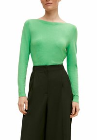 Maglia verde a maniche lunghe in maglia con scollo ampio, abbinata a pantaloni neri a vita alta. Tessuto morbido e design aderente.