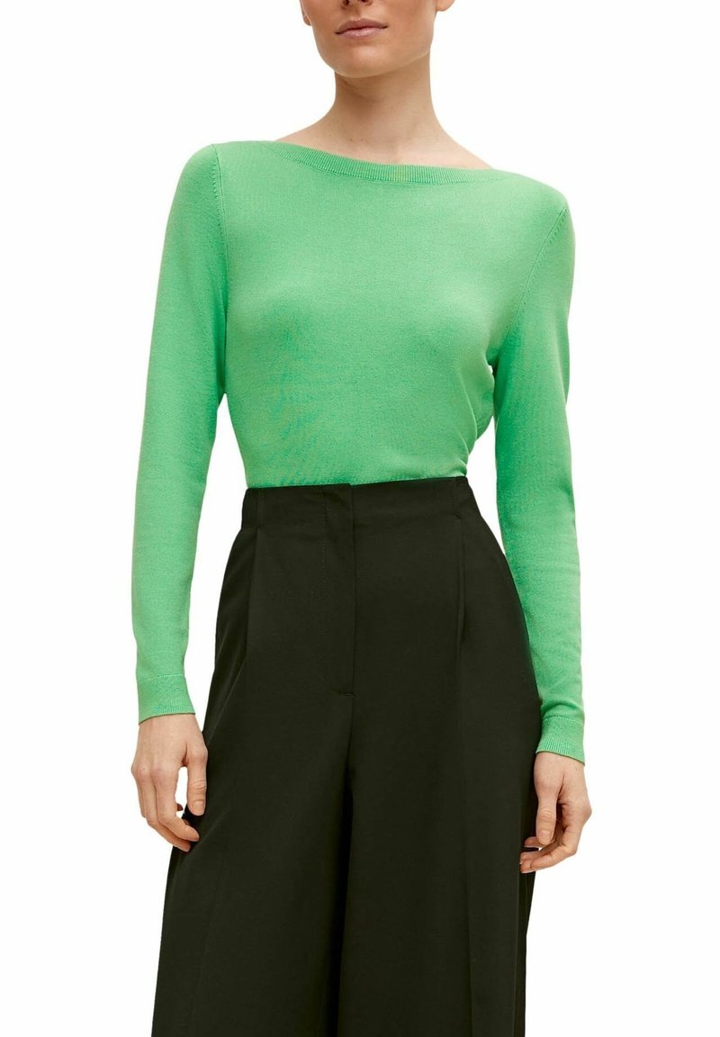 Maglia verde a maniche lunghe in maglia con scollo ampio, abbinata a pantaloni neri a vita alta. Tessuto morbido e design aderente.