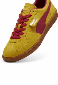 Baskets Puma Palermo en daim jaune avec bande logo bordeaux, lacets bordeaux, marquage doré et semelle en caoutchouc marron.
