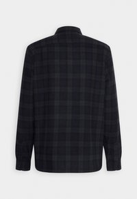 Chemise à carreaux foncés à manches longues vue de dos avec un col et des poignets boutonnés sur fond blanc.
