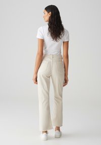 Lichtbeige flared pants met een hoge taille, voorzien van twee achterzakken en onafgewerkte zomen, gecombineerd met een witte aansluitende t-shirt en witte sneakers.