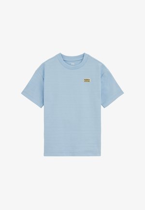 Svetlo modra majica s kratkimi rokavi s majhno bež in črno zastavico "Puerto Montana" na levi strani prsi, rebrastim okroglim ovratnikom in subtilno vodoravno teksturo.