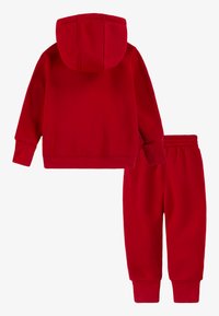 Piros kapucnis pulóver és melegítőnadrág szett puha anyagból. A kapucnis pulóveren kicsi kapucni, bordázott mandzsetták és derékrész található. Végig sima textúrájú.