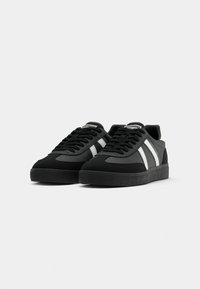 Black low-top sneakers with white stripes on the sides, black laces, and rubber soles, positioned side by side on a white background.