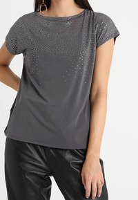 Šedé tečkované tričko s krátkým rukávem, které je na přední straně ozdobeno gradientem skleněných kamenů.