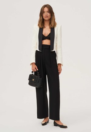 Black and white cropped blazer, black lace bralette, wide black trousers, gold-accented black flats, and a black quilted handbag.