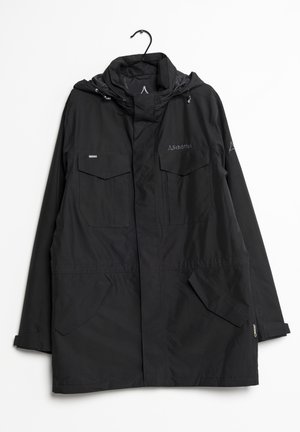 Veste noire imperméable avec capuche, poches avant à rabat, logo Schöffel sur la poitrine et la manche, suspendue à un cintre noir sur fond blanc.
