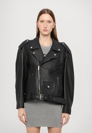 Schwarze Leder-Bikerjacke mit Schulterklappen, Reißverschluss-Taschen und einem geriffelten Bund, getragen über einem grau gestreiften Kleid. Glatte Textur.