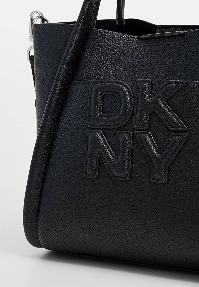 Czarna torebka ze skórki o fakturze pebble z wytłoczonym logo "DK NY". Posiada strukturalny kształt, regulowany pasek oraz metalowe akcenty.