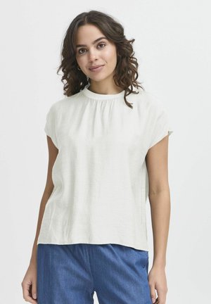 Blouse courte à manches courtes couleur beige clair avec un col rond. Présente des détails froncés au niveau du cou et une coupe décontractée. Fabriquée en tissu texturé.
