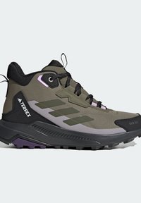 Chaussure de randonnée montante vert olive avec semelle noire, lacets noirs, accents violets et marquée "TERREX" sur le côté du talon.