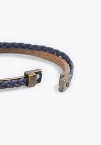 Pulsera de cuero trenzado azul oscuro con parte inferior marrón, que cuenta con dos extremos de cierre magnético de latón antiguo, uno de ellos grabado con un logo.