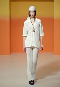 Gehaakte witte top en broek met een open weefpatroon, voorzien van een kraag. Gecombineerd met een zwart-witte ketting en een witte armband.