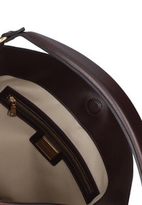 Interno di una borsa in pelle marrone con una fodera beige chiara, dotata di una tasca con zip e un piccolo dettaglio a chiusura a scatto circolare.