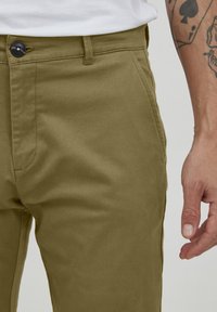 Pantalon sur mesure vert olive en coton. Doté d'une fermeture à bouton à l'avant, de poches latérales et d'une texture lisse avec un design minimaliste.