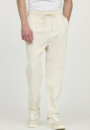Beige gestreepte joggerbroeken met een elastische tailleband en een koord, met een ontspannen pasvorm en opgerolde manchetten. Gecombineerd met witte sneakers.
