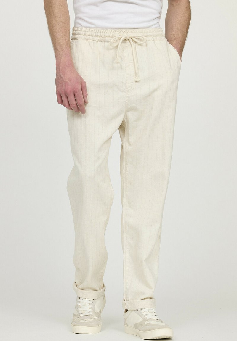 Beige gestreepte joggerbroeken met een elastische tailleband en een koord, met een ontspannen pasvorm en opgerolde manchetten. Gecombineerd met witte sneakers.