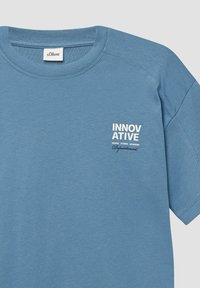 Niebieska bawełniana koszulka z okrągłym dekoltem i krótkimi rękawami. Logo "INNOWACYJNY" w białym kolorze na klatce piersiowej z dodatkowym tekstem poniżej. Gładka faktura.
