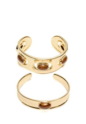 Deux bracelets manchette ouverts en or, chacun avec des pierres ovales marron lisses, l'un plus large avec trois pierres et l'autre plus étroit avec une pierre.