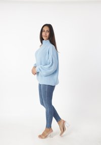 Suéter de punto azul claro con cuello alto, mangas oversized, combinado con jeans de denim ajustados y sandalias de tacón transparente. Diseño simple y texturizado.