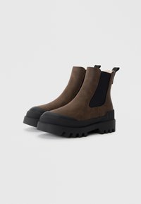 Bottines en cuir marron avec des panneaux élastiques noirs sur les côtés, épais semelles en caoutchouc noir et détails texturés sur le talon.
