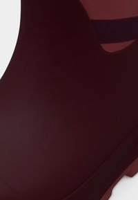 Κοντινή λήψη λείου βυσσινί λαστιχένιου βροχερού μπότες με στρογγυλεμένη μύτη και παχιά σόλα σε λευκό φόντο.