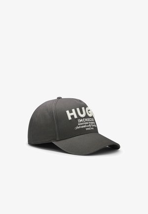 Casquette de baseball gris foncé avec visière courbée et texte brodé blanc "HUGO" ainsi qu'un texte plus petit sur le panneau avant.