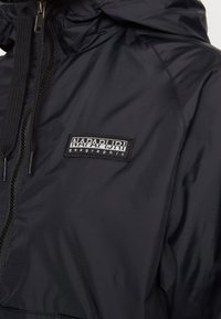 Chaqueta negra con cremallera y capucha, fabricada con material ligero. Presenta un logo en parche y ajuste con cordón. Textura suave con un acabado mate.
